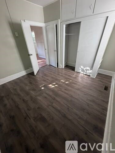 A room with wooden flooring and white walls, with a door open to a hallway.