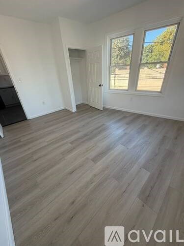 A room with wooden flooring and a window showing trees outside.
