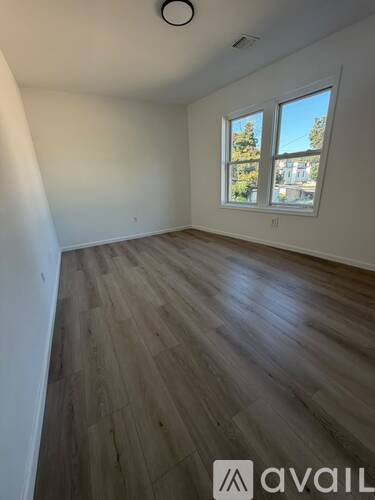 A room with wooden flooring and a window showing trees and a building outside.