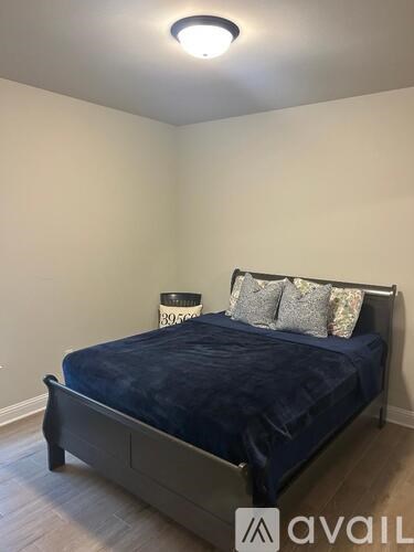 A bed with a dark blue cover and a pillow with a floral pattern is in a room with a white wall and a ceiling light.