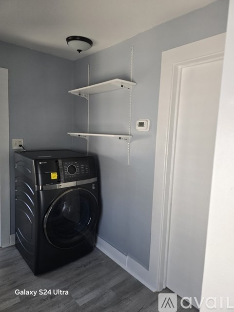 A black washing machine sits in a laundry room with a white door and shelves.