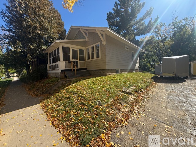 A house with a grey roof and white windows is surrounded by trees and a grassy area with fallen leaves.