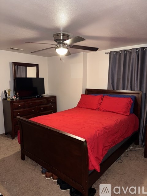A bedroom with a red bed and a ceiling fan.