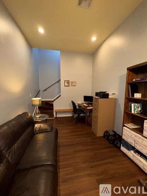A living room with a black leather couch and a wooden bookshelf.