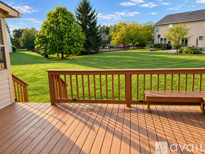A wooden deck with a bench and a view of a green lawn and trees.