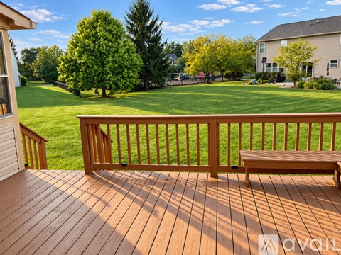 A wooden deck with a bench and a view of a green lawn and trees.