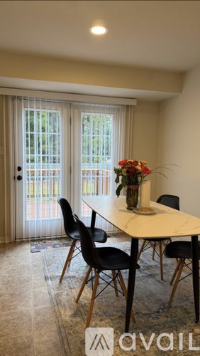 A dining room with a table, chairs, and a vase of flowers.