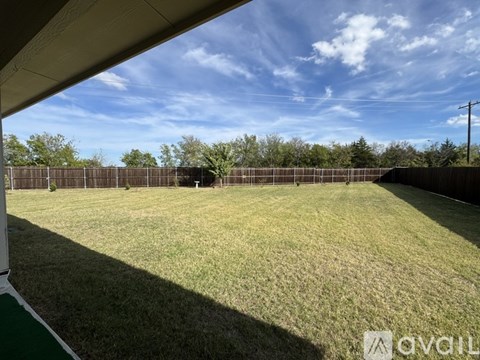 A grassy field with a fence and trees in the distance under a blue sky.