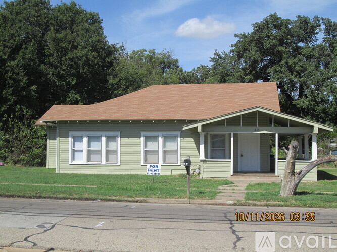 A green house with a brown roof and a sign that says "FOR RENT" in front of it.