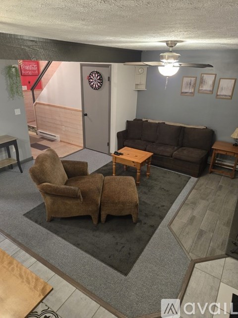 A living room with a brown couch, a brown chair, and a dartboard on the wall.