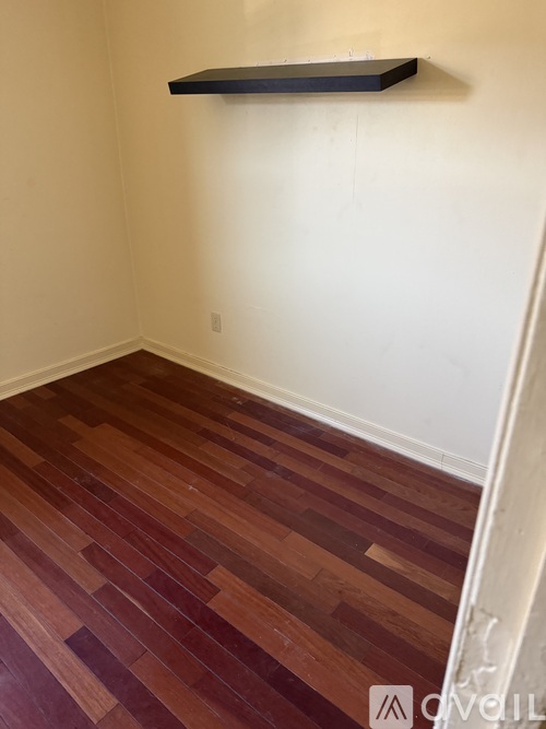 A room with a wooden floor and a black shelf on the wall.