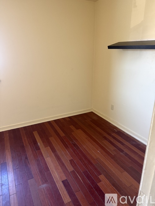 A room with wooden flooring and a black shelf on the wall.