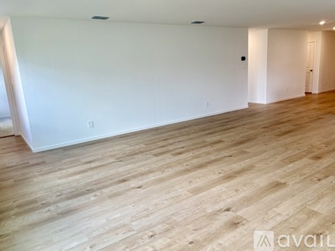 A spacious room with wooden flooring and white walls.