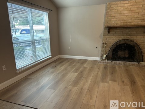 A room with wooden flooring and a fireplace with a brick wall above it.