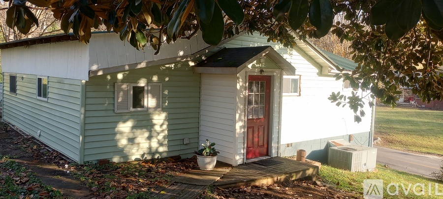 A small white house with a red door is surrounded by trees.