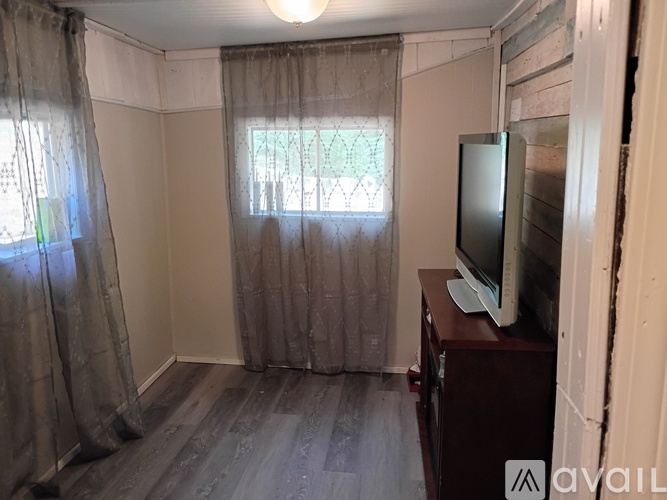 A room with a television on a stand and a window with curtains.