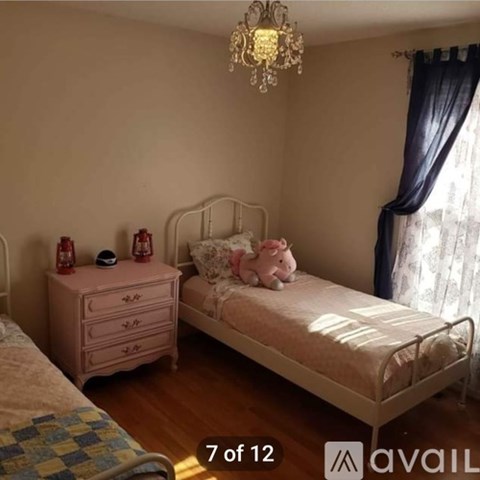 A bedroom with a white bed and a pink dresser with a chandelier hanging from the ceiling.