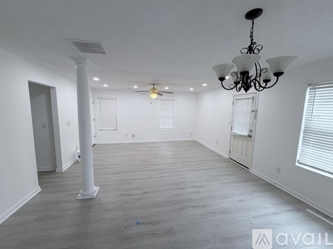 A spacious room with a chandelier, a pillar, and a ceiling fan.