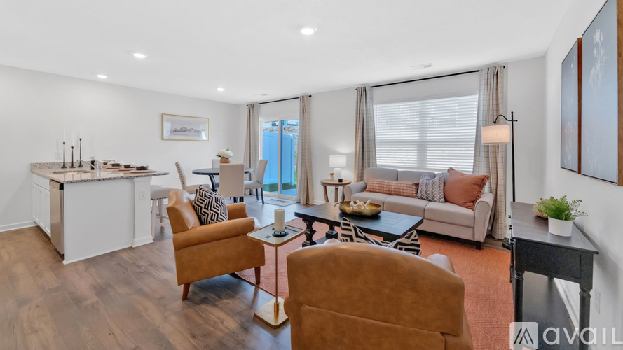 A living room with a brown sofa and a white kitchen area.