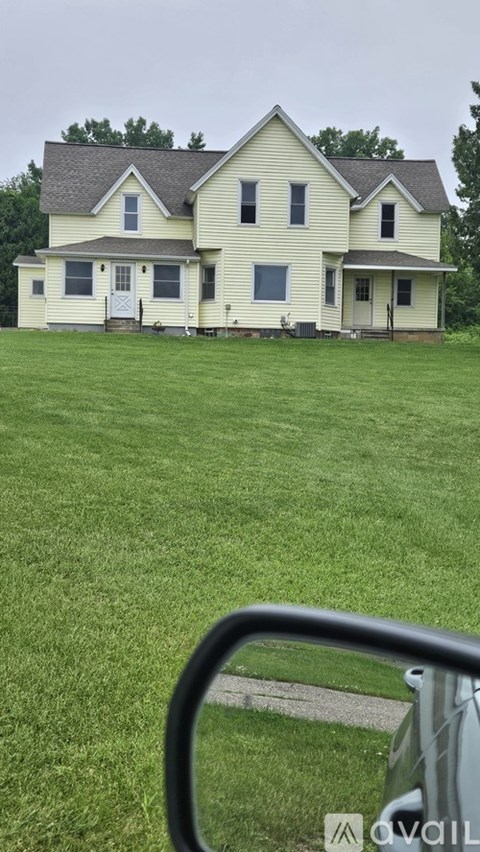 A house with a white and yellow exterior is surrounded by a green lawn.
