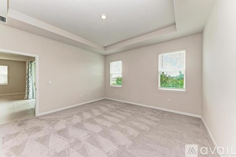 A spacious room with a carpeted floor and two windows.