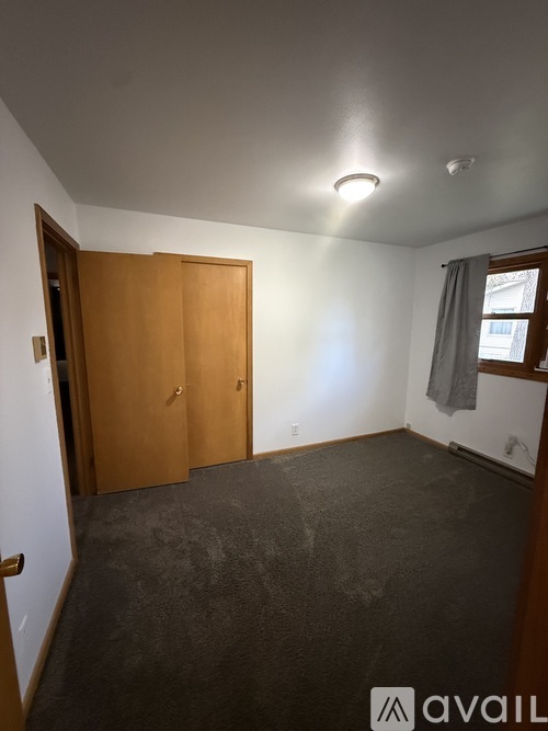 A room with a carpeted floor and a window with a grey curtain.