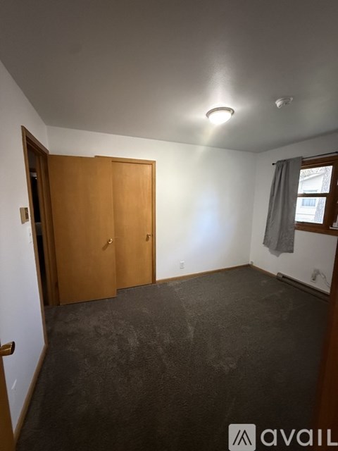 A room with a carpeted floor and a window with a grey curtain.