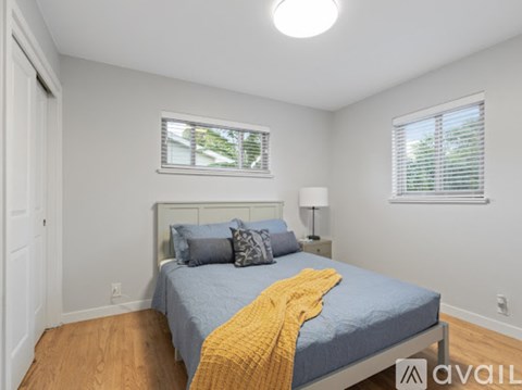 A bedroom with a bed, a window with blinds, a nightstand with a lamp, and a yellow throw blanket.