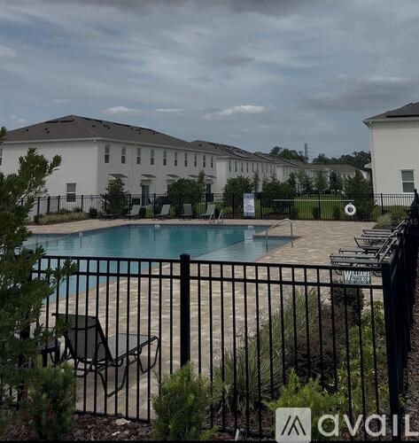 A pool surrounded by a black fence with chairs and plants in front.