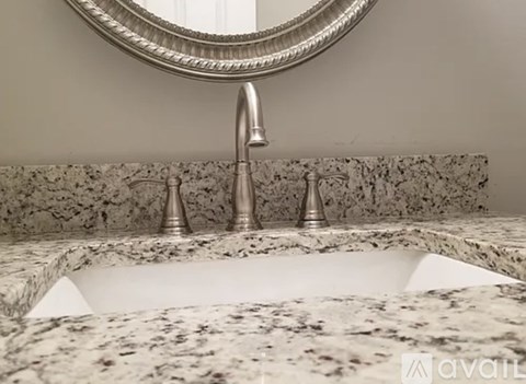 A bathroom sink with a marble countertop and a round mirror above it.