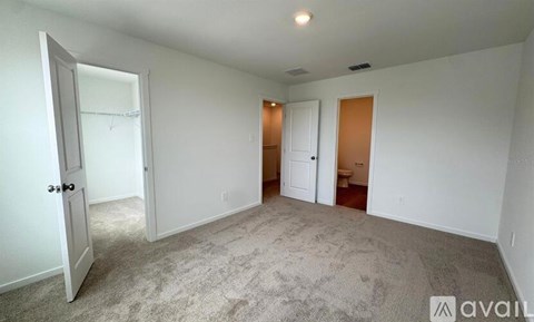 A room with a carpeted floor and white walls, with a door on the left and a toilet in the corner.