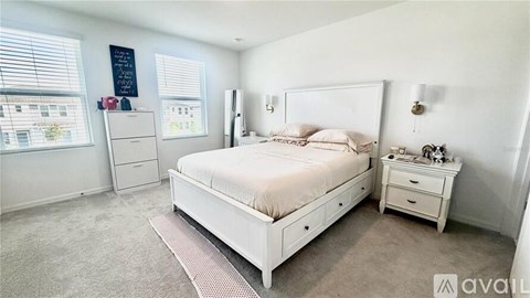 A white bedroom with a large bed, nightstand, and window.