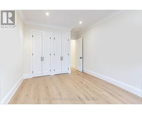 A room with a white wall and wooden floor with a set of white cupboards.