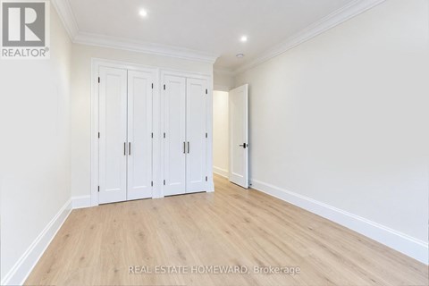 A room with a white wall and wooden floor with a set of white cupboards.