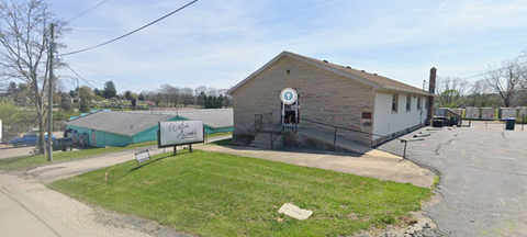 A small building with a sign on it is surrounded by a fence and a grassy area.