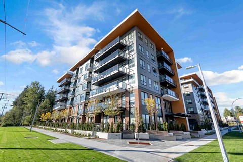 A modern multi-story residential building with balconies and a landscaped front yard.
