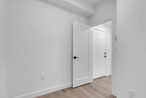 A white door is in a hallway with wood floors and white walls.