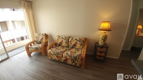 A living room with a floral couch and matching chair, a lamp on a side table, and a large window with curtains.