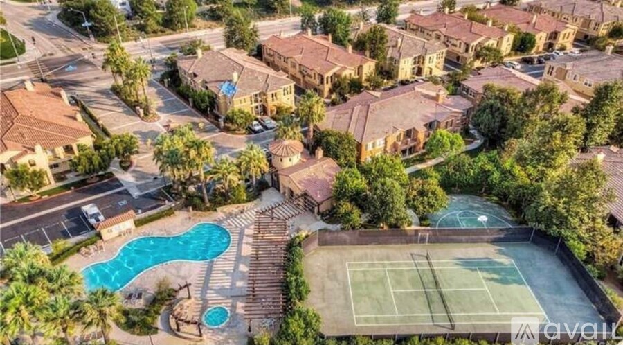 A tennis court is surrounded by a pool and palm trees in a gated community.