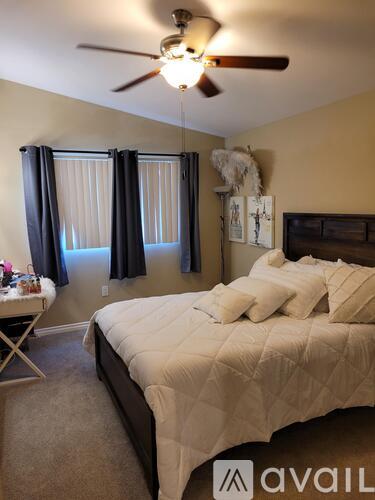 A bedroom with a bed, a ceiling fan, and a window with black curtains.