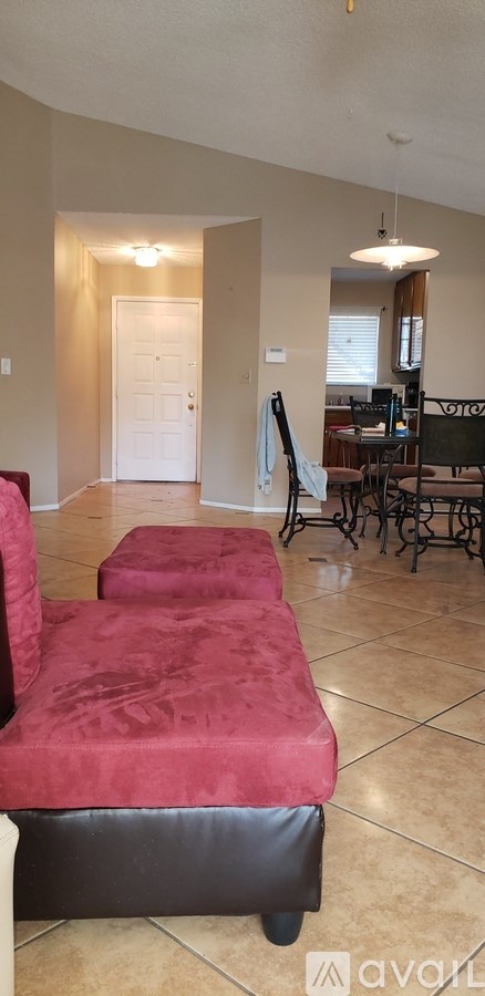 A living room with a red couch and a dining area in the background.
