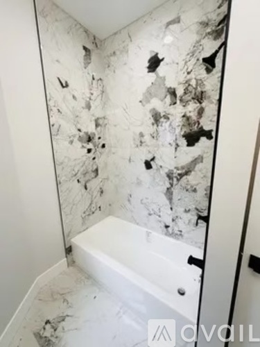 A bathroom with a white tub and marble wall tiles.