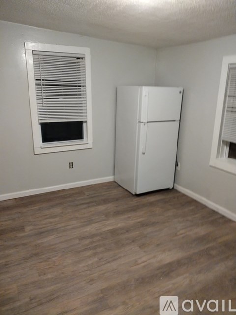 A white refrigerator in a room with wooden flooring and a window with blinds.