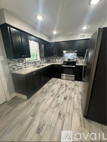 A kitchen with black cabinets and a wooden floor.