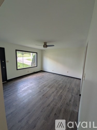 A room with wooden flooring and a window overlooking a green area.