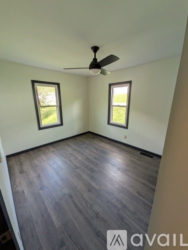 A room with a ceiling fan and two windows.