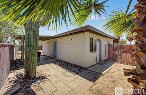 A house with a blue door is surrounded by a fence and has a palm tree in front.