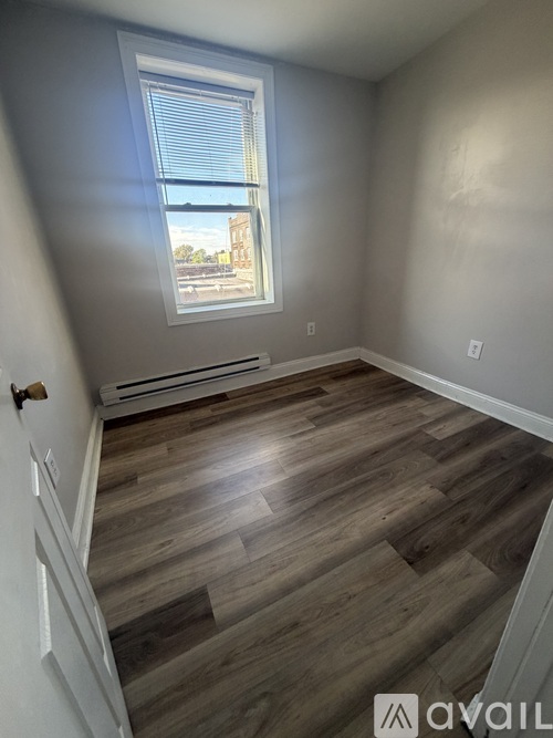 A room with wooden flooring and a window overlooking a building.