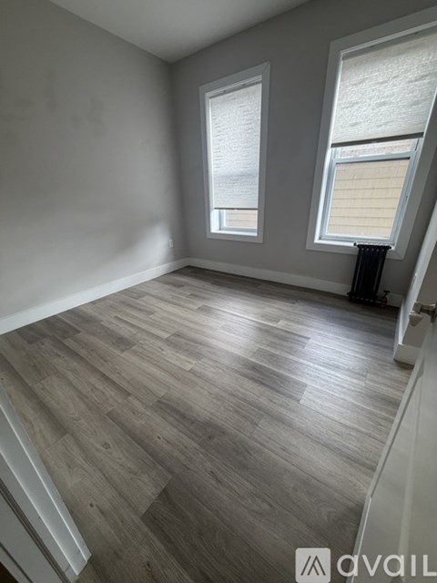 A room with wooden flooring and two windows.