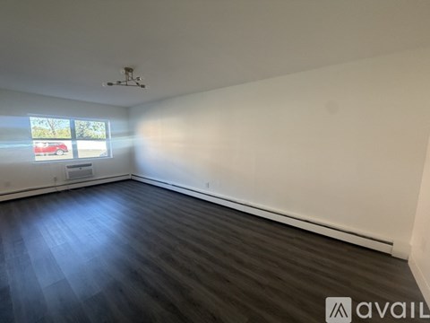 A room with wooden flooring and a window showing a red car and trees outside.